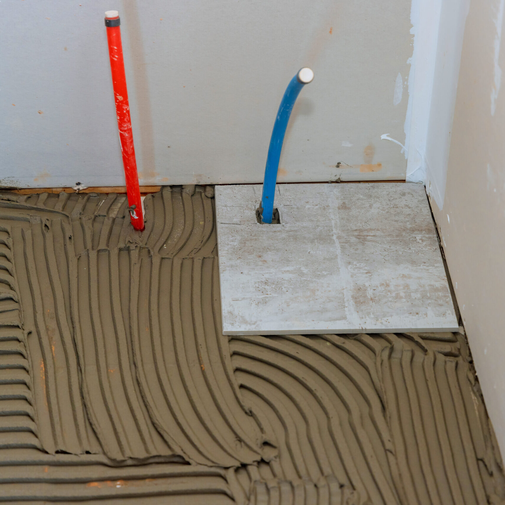 Ceramic tile is being placed over adhesive on bathroom floor by tiler